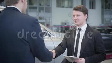 褐发白种人蓝眼睛交易员穿着商务服的画像摇着客户的手和谈话。 年轻汽车经销商